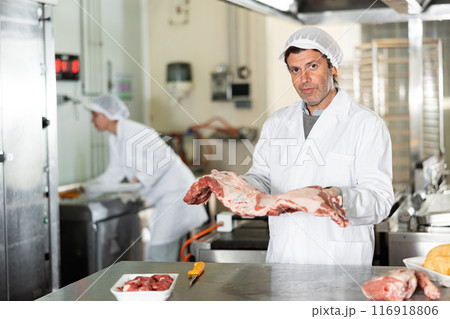 Male kitchen worker closely examines meat for cutting and preparing for sale 116918806