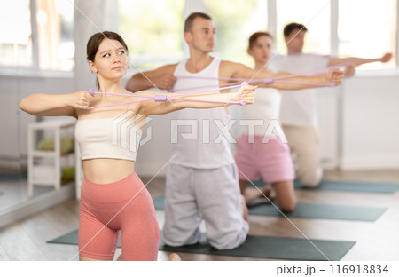 Young girl doing arm workout with resistance band standing on knees 116918834