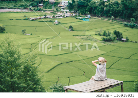 Rear view of tourist woman looking to beautiful rice paddy field in Sapan village a small village nestled in a forested northern valley of pure air and pristine rivers in Nan province of Thailand. Rear view of tourist woman looking to beautiful rice paddy field in Sapan village a small village nestled in a forested northern valley of pure air and pristine rivers in Nan province of Thailand. 116919933