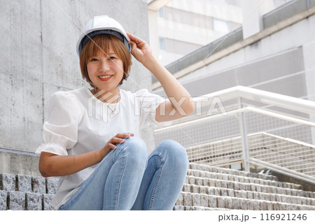 コンクリートの建物と階段を背景にヘルメットをかぶった女性が笑っている 116921246