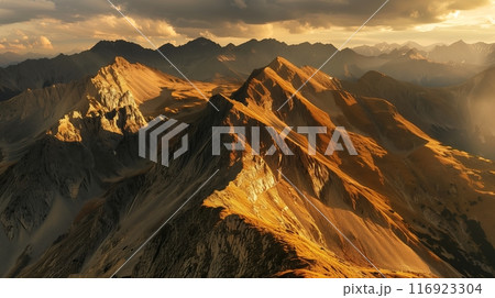 Golden sunlight illuminates jagged mountains, casting shadows and highlighting the rugged, stunning view. 116923304