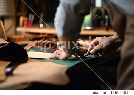 Close up view of craftsman skillfully using a cutting tool to shape the leather 116925699