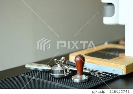Coffee making tools. Espresso machine, portafilter and tamper arranged neatly on a black rubber mat Coffee making tools. Espresso machine, portafilter and tamper arranged neatly on a black rubber mat 116925741