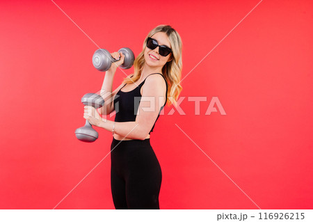 Young fitness trainer instructor wear black top hold dumbbells isolated on red background. Young fitness trainer instructor wear black top hold dumbbells isolated on red background. 116926215