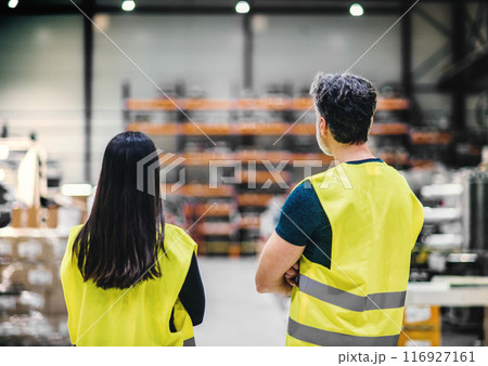 Warehouse employee in warehouse. Male worker in reflective clothing in modern industrial factory, heavy industry, manufactrury. Rear view. 116927161