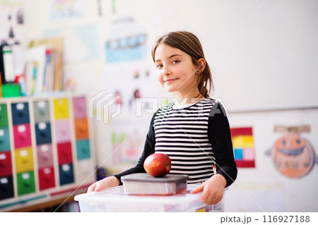 Portrait of schoolgirl, pupil sitting at desk in classroom at the elementary school. Student girl holding apple during snack time, break 116927188