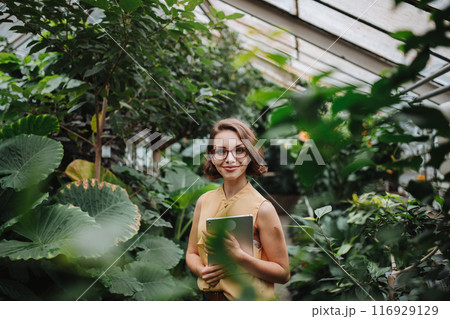 Beautiful woman standing in botanical garden, in the middle of lush green foliage. 116929129