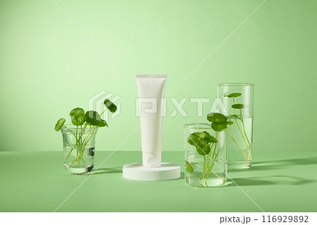 Mock up for cosmetic advertising with an unbranded white tube featured on green background, placed next to some glass beaker, which containing transparent liquid and centella asiatica 116929892