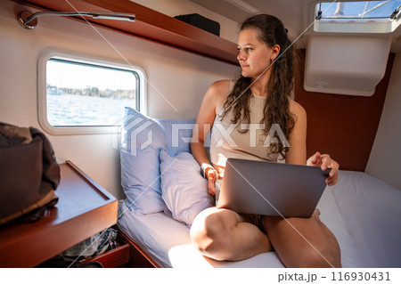 Young woman freelancer using laptop and looking out the window in the cabin of a yacht during sailing in sea. Yacht life concept Young woman freelancer using laptop and looking out the window in the cabin of a yacht during sailing in sea. Yacht life concept 116930431