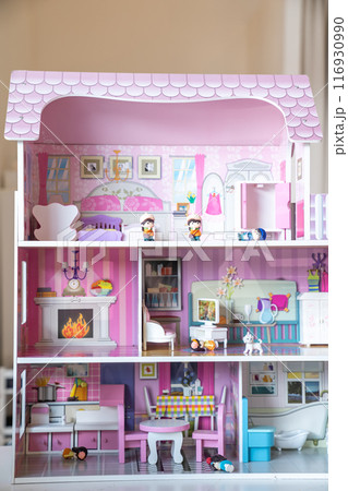 The photo of huge pink dollhouse model furnished with miniature furniture in a kids room. The photo of huge pink dollhouse model furnished with miniature furniture in a kids room. 116930990