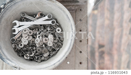 A bucket full of wrenches, washers and stud bolts is placed on the scaffolding. 116931043
