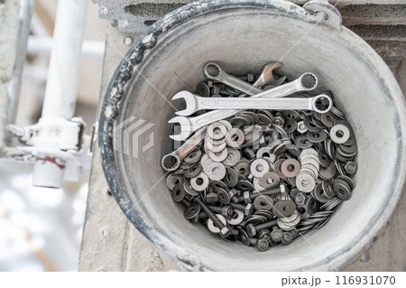 A bucket full of wrenches, washers and stud bolts is placed on the scaffolding. 116931070