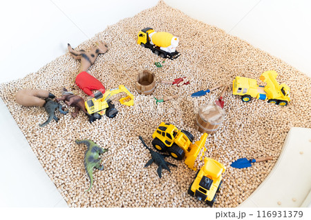 Yellow construction toy vehicles and Dinosaurs Toys are placed in kid playground filled with wooden cubes around it. Yellow construction toy vehicles and Dinosaurs Toys are placed in kid playground filled with wooden cubes around it. 116931379