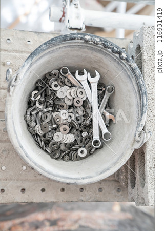 A bucket full of wrenches, washers and stud bolts is placed on the scaffolding. 116931419