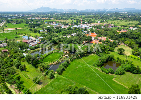 Drone view of Sufficiency Economy, Land full of agricultural activities with green rice fields, big ponds, and trees. Small houses and temple close by a pond. 116931429