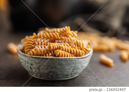 Uncooked whole grain pasta. Fusilli pasta in bowl on black kitchen table. Uncooked whole grain pasta. Fusilli pasta in bowl on black kitchen table. 116932407