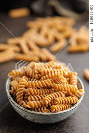 Uncooked whole grain pasta. Fusilli pasta in bowl on black kitchen table. Uncooked whole grain pasta. Fusilli pasta in bowl on black kitchen table. 116932409
