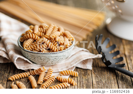 Uncooked whole grain pasta. Raw fusilli pasta in bowl on wooden table. 116932416
