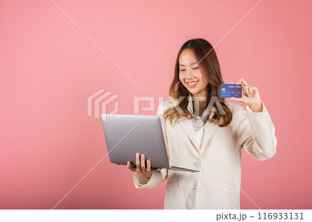 Portrait of Asian beautiful young woman customer showing credit card for online payment shopping transactions cashback loan on laptop studio shot isolated on pink background 116933131