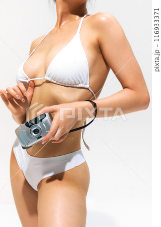 Sensual memories. Cropped image of female body, woman wearing white swimsuit, posing with retro camera against light background 116933371