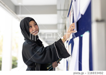 Muslim student in university smiling wearing black niqab finding job looking at the billboard. Arab black chador lady. 116933492