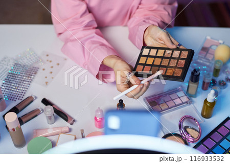 Top view closeup of young woman as beauty influencer recording makeup tutorial focus on hands holding palette with glittering eyeshadow copy space Top view closeup of young woman as beauty influencer recording makeup tutorial focus on hands holding palette with glittering eyeshadow copy space 116933532