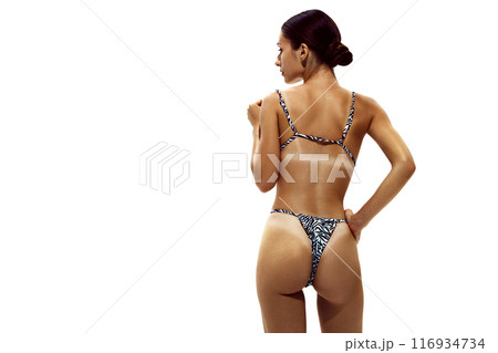 Woman stands in zebra-print bikini, showing off her deeply tanned skin and distinct tan lines against white studio background. 116934734