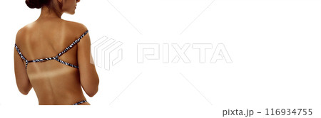 Banner. Woman adjusts bikini, showing distinct tan lines on her deeply tanned skin against white studio background with negative space to insert text. 116934755