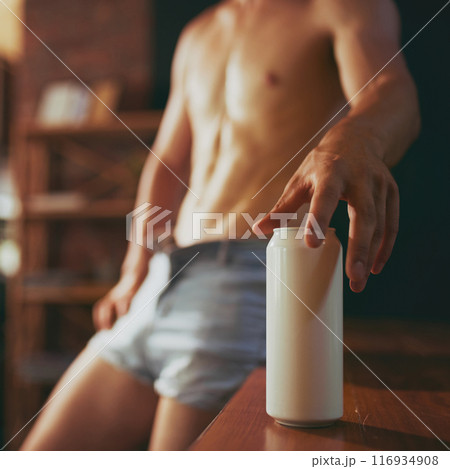 Shirtless, man with athletic body in denim jeans leaned on bar counter and reaching to can of refreshing beer at pub. 116934908