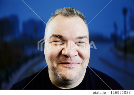 Shy smile of overweight European man in her 40s, face closeup on blue background. 116935088