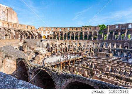 A scenic view of the Colosseum in Rome, Italy, during sunset. The ancient amphitheater is bathed in golden light, with crowds of people enjoying the warm evening. 116935183