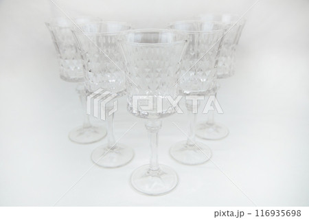 Crystal wine glasses with expanded edges and faceted pattern stand in a wedge on a white background close-up. High quality photo Crystal wine glasses with expanded edges and faceted pattern stand in a wedge on a white background close-up. High quality photo 116935698