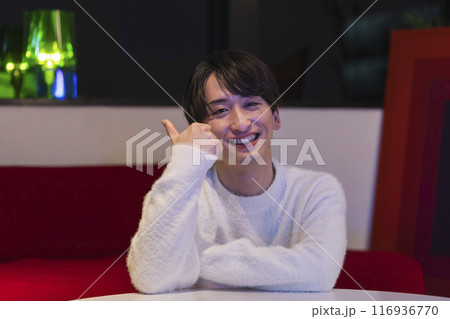 カメラ目線でサムアップをする笑顔の若い男性　自宅　夜　イメージ 116936770
