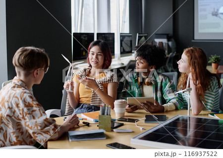 Multi-ethnic group of modern teenagers sitting at table in classroom discussing renewable energy technologies Multi-ethnic group of modern teenagers sitting at table in classroom discussing renewable energy technologies 116937522
