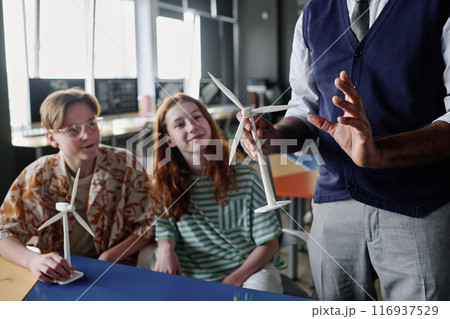Selective focus shot of unrecognizable teacher holding wind turbine model telling teenagers about renewable energy 116937529