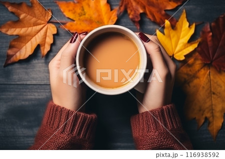 Female hands holding a cup of coffee with autumn leaves on the table 116938592