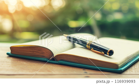 Open Journal with Pen on Wooden Table in Sunlit Outdoor Setting 116939093