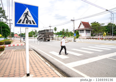 An Asian man prepares himself to walk and run across crosswalk to the other side, Thailand. An Asian man prepares himself to walk and run across crosswalk to the other side, Thailand. 116939136