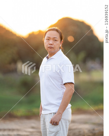 Asian Man long hair stands and relax on the dry field in golden twilight time. 116939152