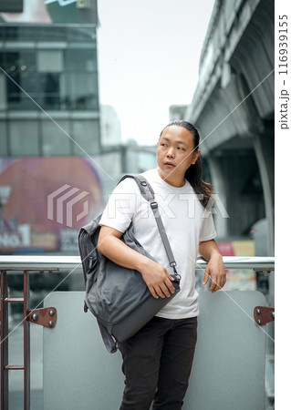 Long Hair Thai, Chinese man is posing in front of the terrace barricade with gray back on the shoulder at outdoor building environment 116939155