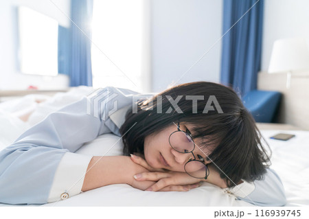 Asian young glasses woman lie on her side on the bed in the morning. 116939745