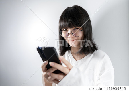 Isolated Pretty Asian glasses woman looks at camera and holds mobile phone in her hand on white background in studio light. Isolated Pretty Asian glasses woman looks at camera and holds mobile phone in her hand on white background in studio light. 116939746
