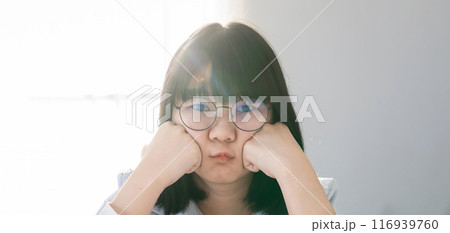 Pretty Asian Woman pucker up her lip in front of the bed in hotel bedroom, with the light from window curtain behind her. Pretty Asian Woman pucker up her lip in front of the bed in hotel bedroom, with the light from window curtain behind her. 116939760