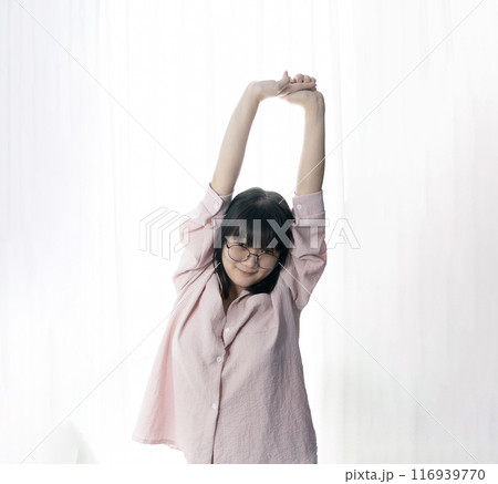 Standed Little Asian young Glasses Girl stretches oneself in front of light white curtain background. 116939770