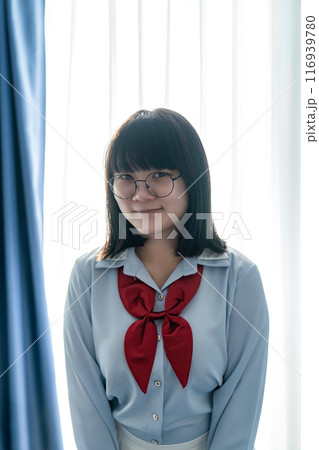 Asian glasses cute woman in blue shirt beside the curtain and window light in bedroom. 116939780