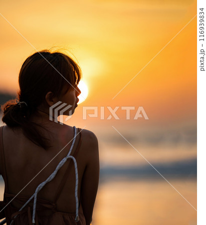 Asian Woman in Silhouette mood and tone of picture with orange warm sunset blurs, background on Kata Beach, Phuket province, Thailand. Asian Woman in Silhouette mood and tone of picture with orange warm sunset blurs, background on Kata Beach, Phuket province, Thailand. 116939834