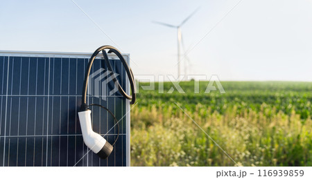 Close up of electric car charging plug with solar panel. Wind turbines in the background 116939859