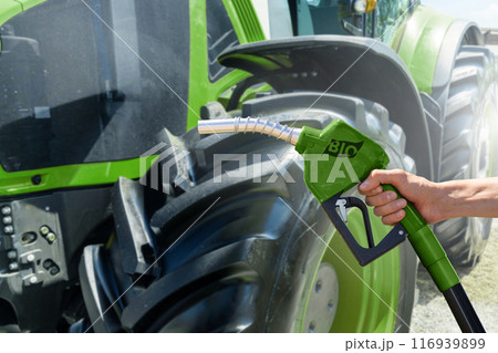 Hand with biofuel refueling nozzle on a background of agricultural tractor Hand with biofuel refueling nozzle on a background of agricultural tractor 116939899