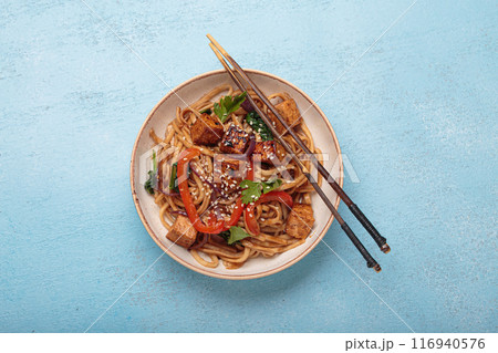 Bowl of vegetarian udon noodles with fried tofu and vegetables is served with chopsticks Bowl of vegetarian udon noodles with fried tofu and vegetables is served with chopsticks 116940576