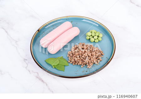 Sausages garnished with boiled buckwheat, green peas and basil leaves. 116940607